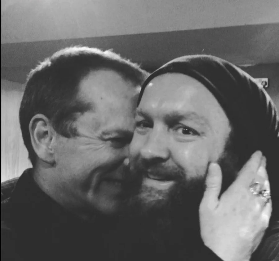 Close-up black-and-white photograph of Kiefer Sutherland and Nathan Clark, cheek to cheek and smiling